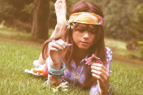 Девушка хиппи лежит на траве, в руке держит цветок