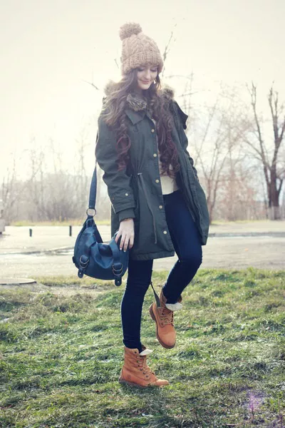Девушка в джинсах, тимберлендах и куртке с шапкой с помпоном на голове