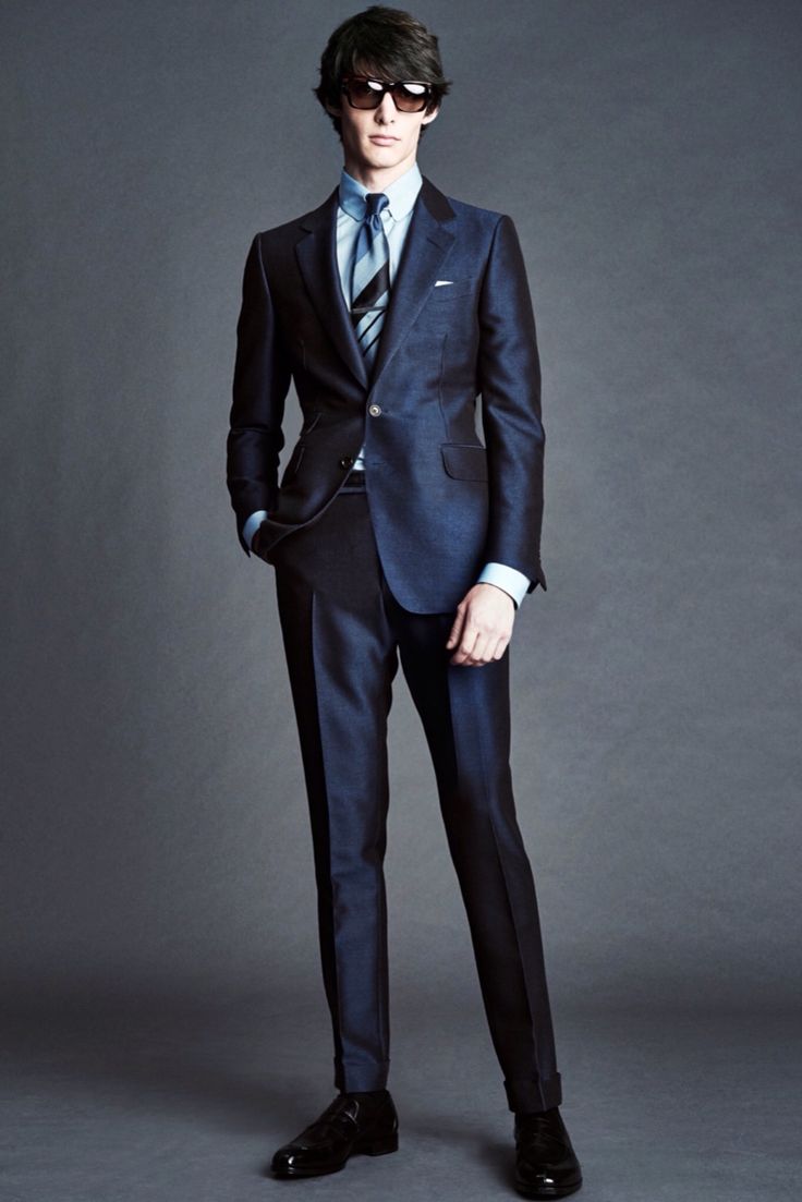 Модель в костюме темного цвета, зауженные брюки, галстук в полоску