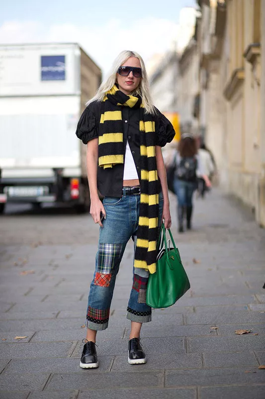 Девушка в джинсах с заплатами, черной блузе и полосатым шарфом