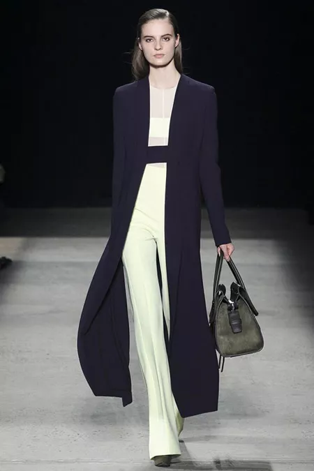 Модель в белых расклешенных брюках со стрелками и длинное черное пальто