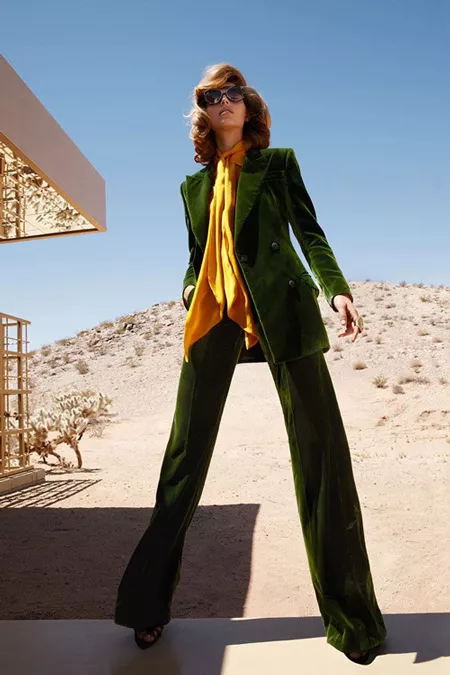 Модель в брючном костюме зеленого цвета с ярком желто оранжевым платком