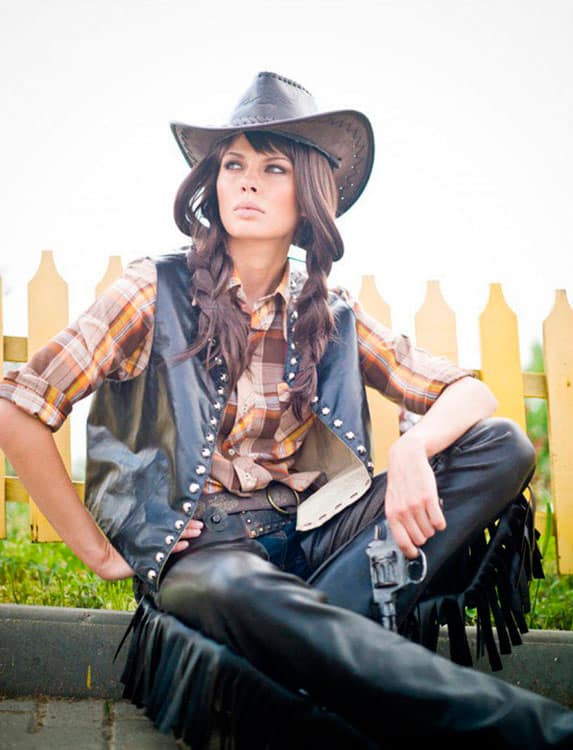 Девушка в кожаных штанах с бахромой, кожаной жилетке и ковбойской шляпе