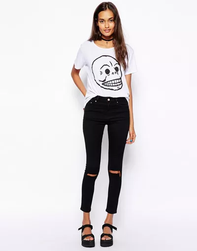Девушка в черных рваных джинсах и белой футболке с принтом