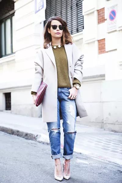 Девушка в рваных джинсах, джемпере и светлом пальто