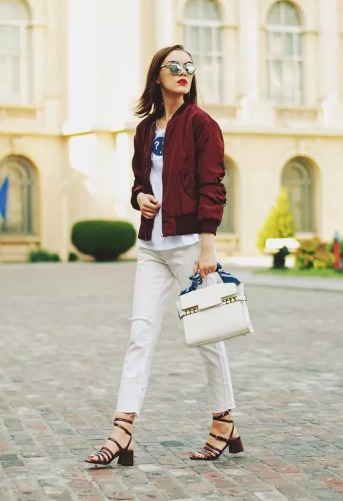 Девушка в белых джинсах, босоножках и бордовом бомбере