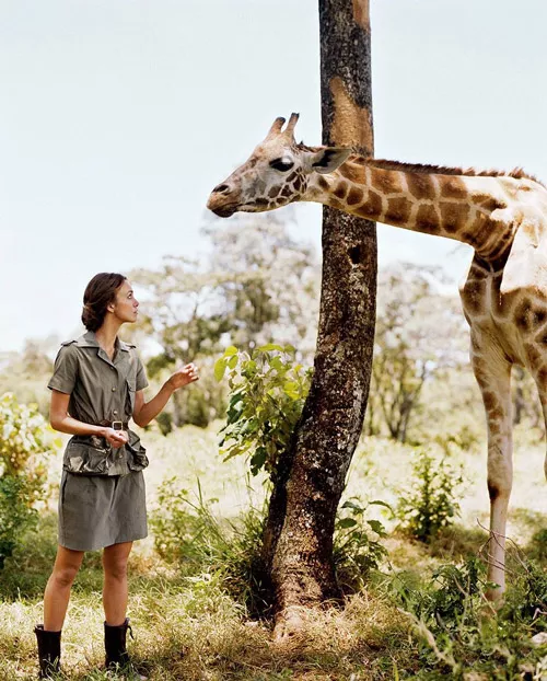 Девушка в платье в стиле сафари стоит рядом с жирафом