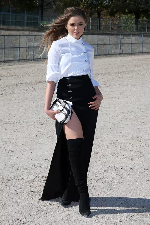 Модель в черных сапогах выше колен, черной макси юбке с вырезом и белой блузе