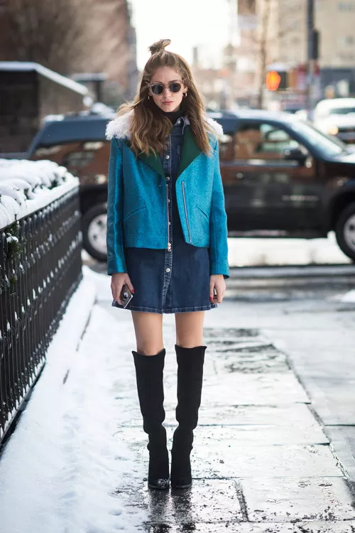 Модель в черных сапогах выше колен, джинсовом платье и голубой куртке