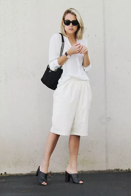 Девушка в белых бермудах, блузе и черные босоножки и сумочка