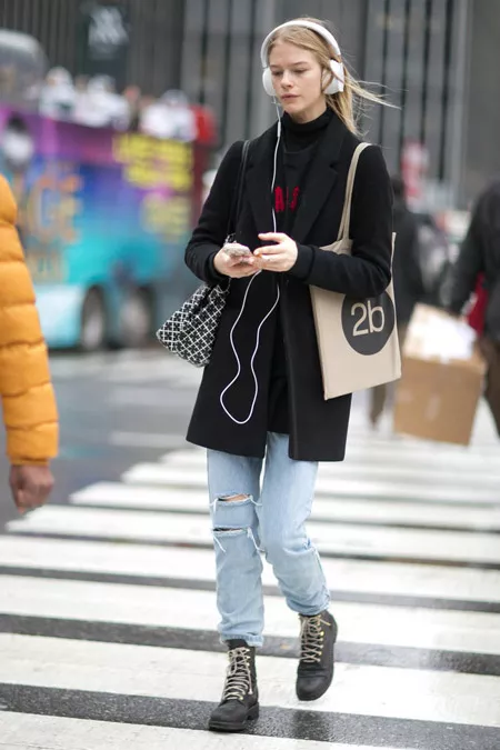 Девушка в рванных джинсах. ботинках на шнуровке и черном пальто пямого кроя