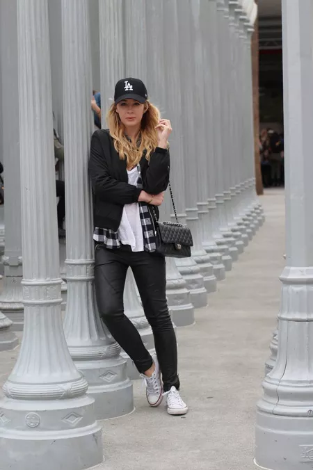 Девушка в черных брюках, белая футболка, черная куртка, кроссовки и кепка