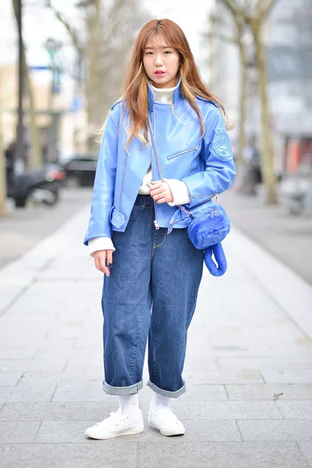 Девушка в широких джинсах, голубой кожаной куртке, белые кроссовки и водолазка