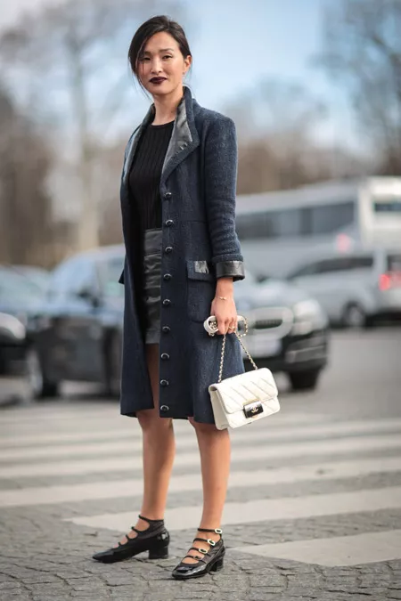 Модель в мини юбке, черной футболке и пальто, белая сумочка