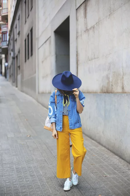 Модель в желтых брюках, тельняшке, джинсовая куртка и синяя шляпа