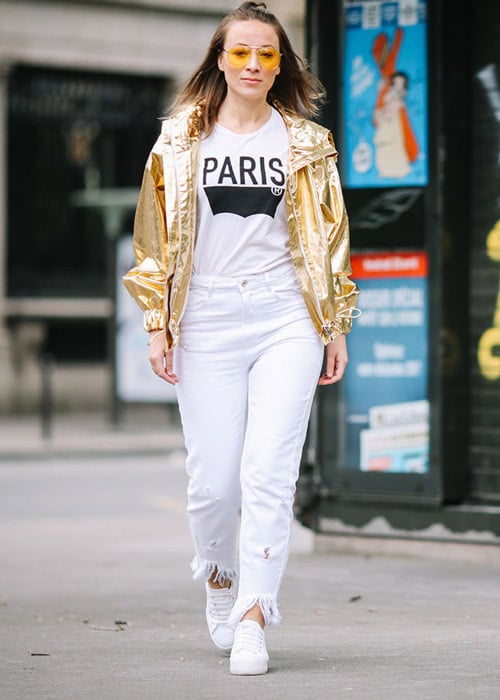 Девушка в белых джинсах, футболке с принтом и золотистой куртке