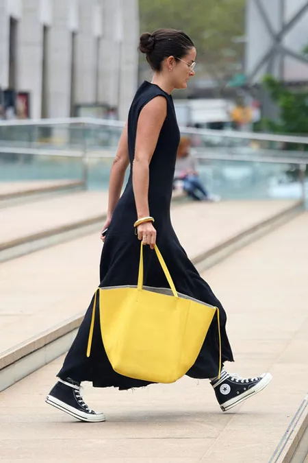 Девушка в в черном макси платье, кедах и с желтой сумкой тоут