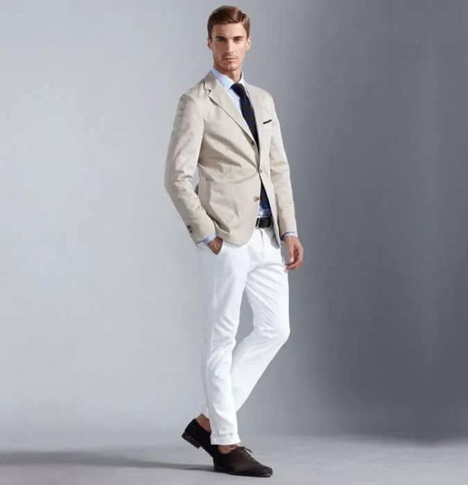 Мужчина в белых джинсах, сером блейзере и коричневых ботинках