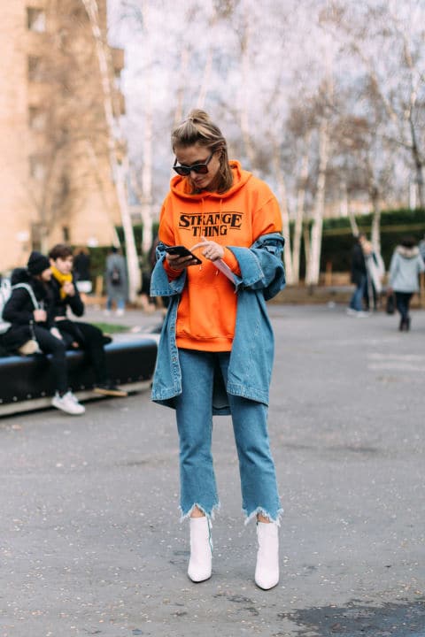 Девушка в оранжевой толстовке, синих джинсах и белых ботильонах