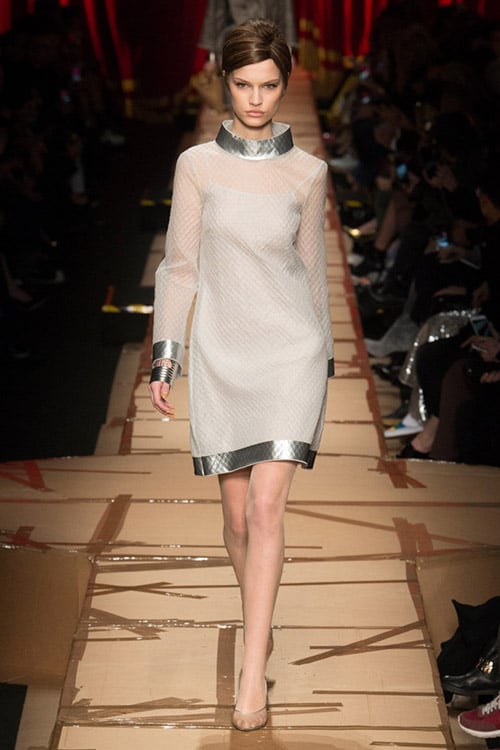 Модель в белом платье с серебристой отделкой и выше колен от Moschino