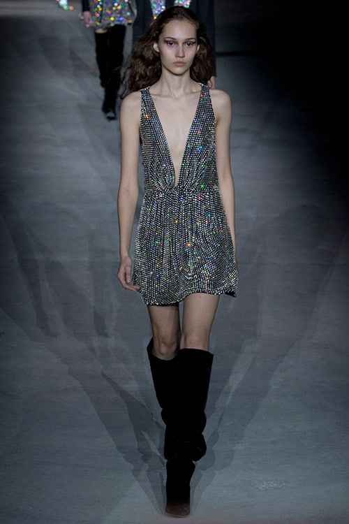 Модель в серебристом мини платье с глубоким декольте от Saint Laurent