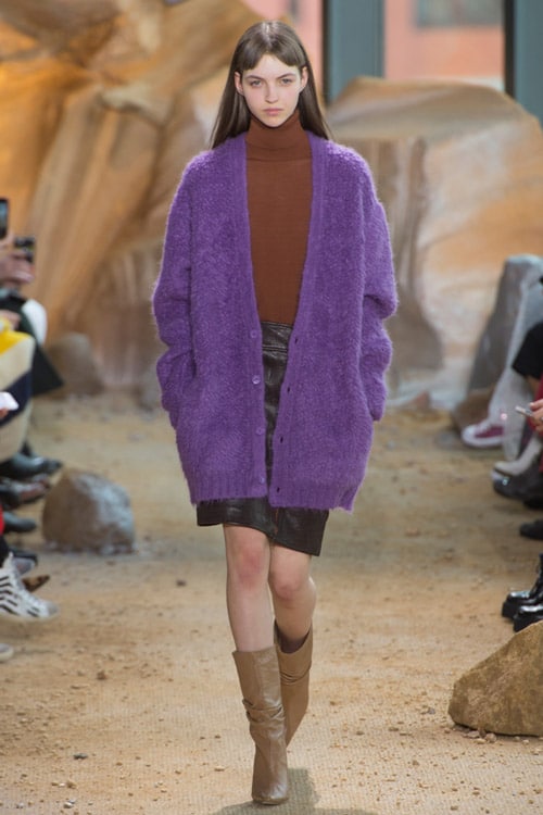 Модель на показе Lacoste в кожаной юбке, сапогах и фиолетовом кардигане