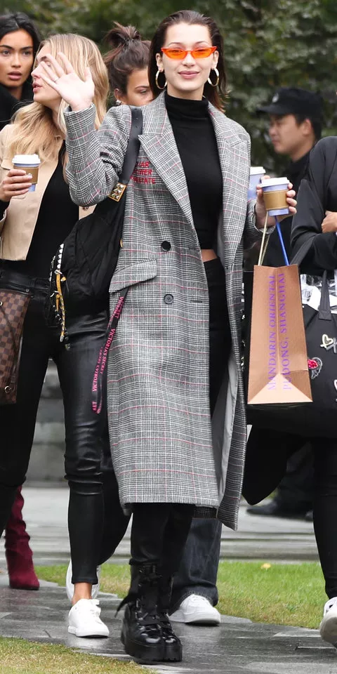 Белла Хадид в черных джинсах, топе и ботинках. Заверщают образ клетчатое пальто и очки