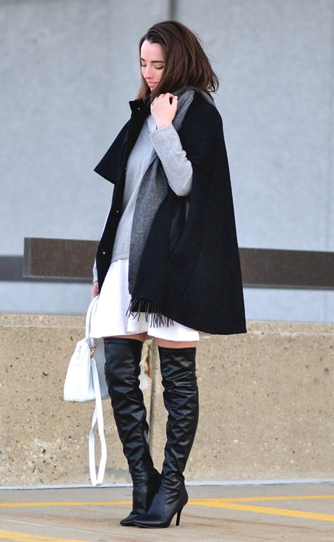 Девушка в ботфортах на шпильке, черное пальто и белая мини юбка