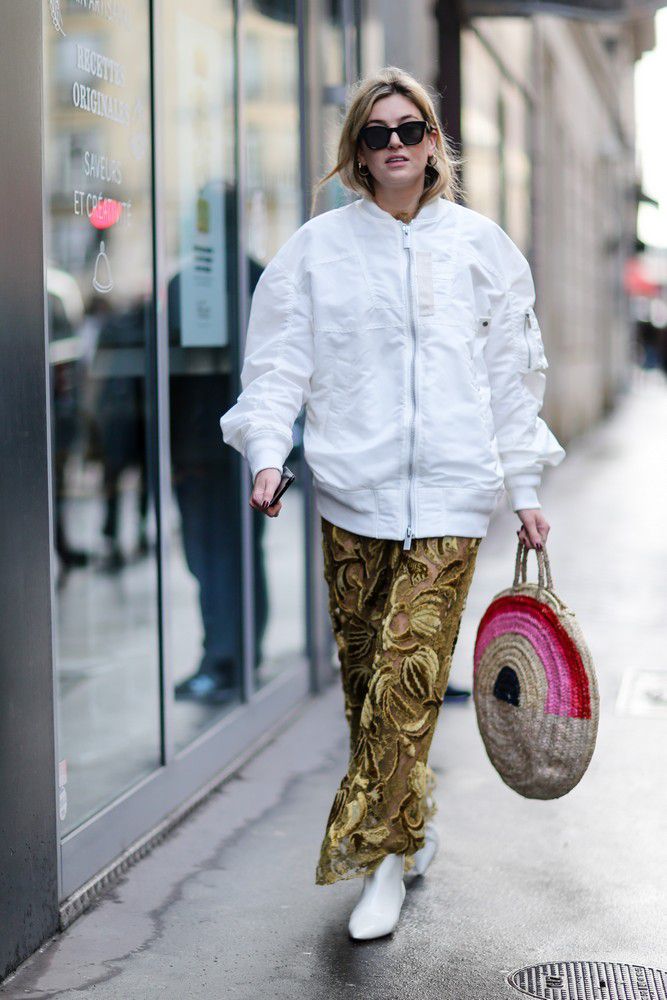 Девушка в золотых брюках, белая куртка и круглая соломенная сумка
