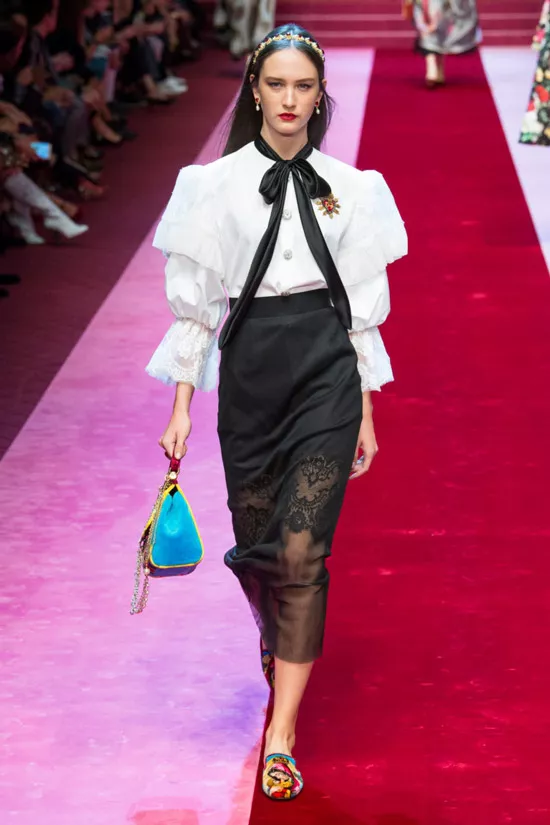 Модель в белой блузке с пышнами рукавами и черным бантом, черная узкая юбка от Dolce & Gabbana