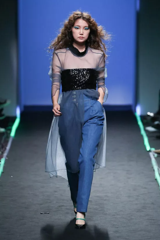 Модель в синих джинсах и черной прозрачной блузке от Fleamadonna