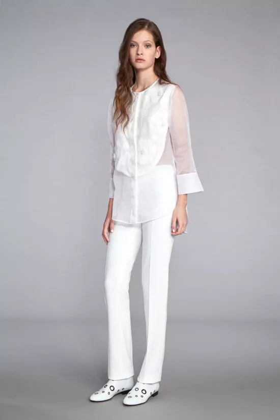Модель в удлиненной белой блузке без воротника и белых брюках от Kiton