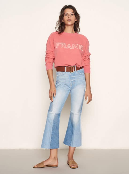 Модель в укороченных джинсах клеш с ремнем и розовая толстовка от Frame Denim