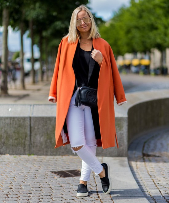 Девушка в рваных белых джинсах и оранжевом пальто