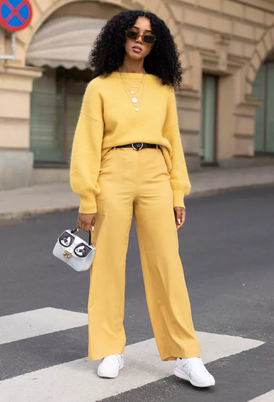 Девушка в желтых брюках палаццо, желтый свитер и белые кроссовки