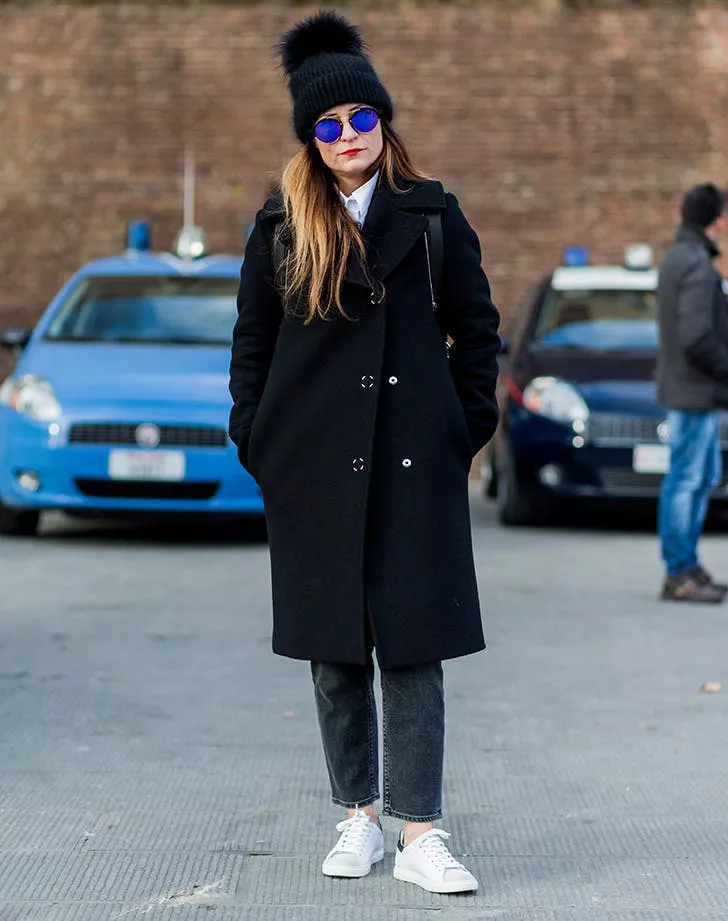 Девушка в черном пальто, шапка, серые джинсы и белые кеды