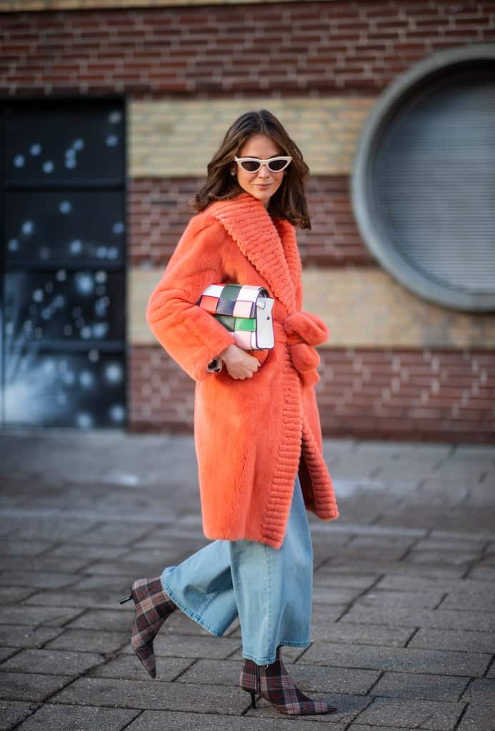 Девушка в оранжевом меховом пальто, широкие джинсы и ботильоны в клетку