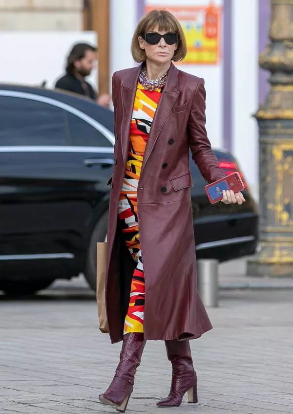 Анна Винтур в бордовом кожаном плаще, яркое платье и высокие сапоги