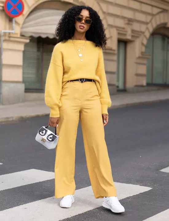 Девушка в желтых брюках, желтый свитер, белые кроссовки и сумочка