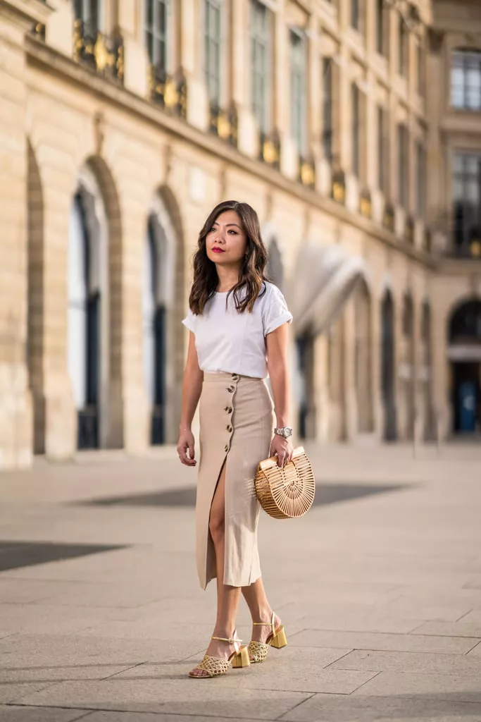 Девушка в облегающей юбке миди, белая футболка и деревянная сумка