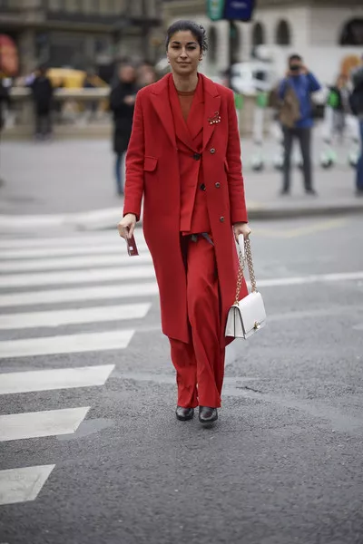 Девушка в красном брючном костюме, пальто и белая сумочка