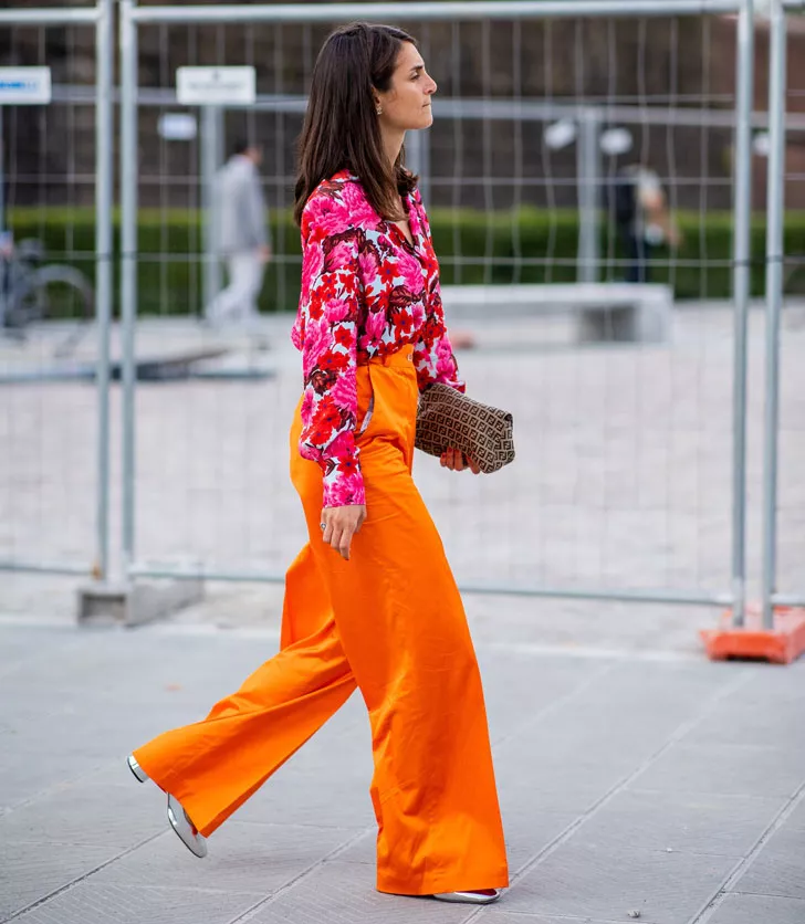 женщина в оранжевых брюках, блузе в цветочек и серебристой обуви