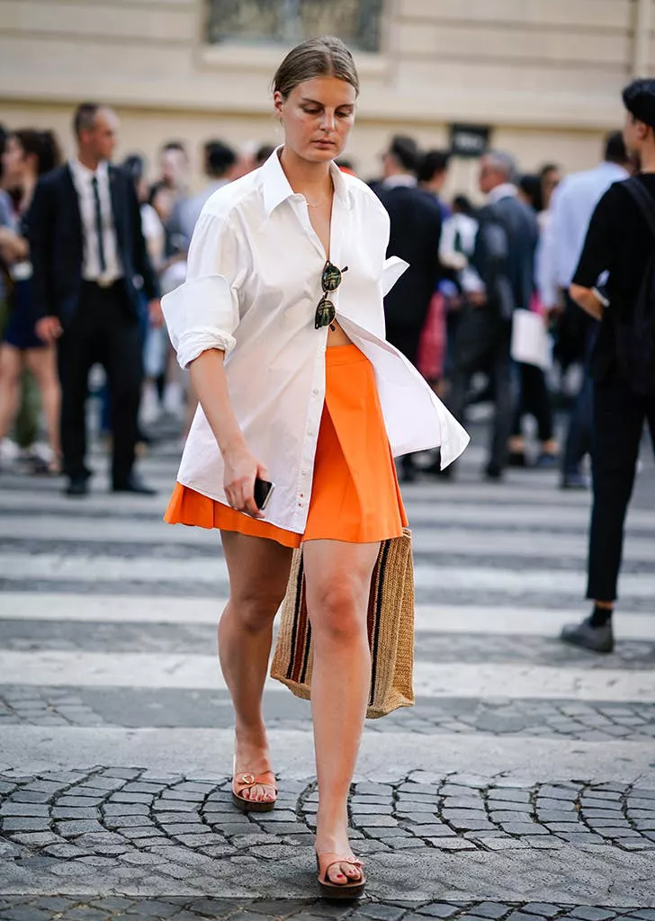 Девушка в оранжевой юбке мини, белая рубашка оверсайз и сандалии