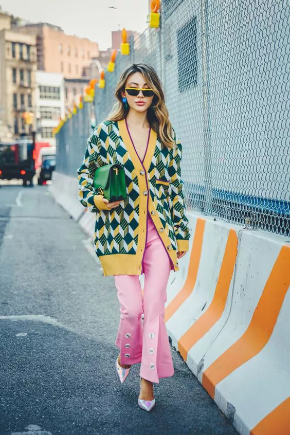 Девушка в розовых брюках клеш, желто-зеленый кардиган в ромбик и зеленая сумка