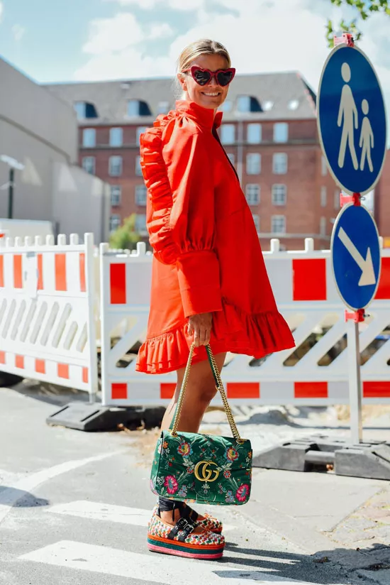 Девушка в свободном красном платье, сандалии на платформе и зеленая сумка