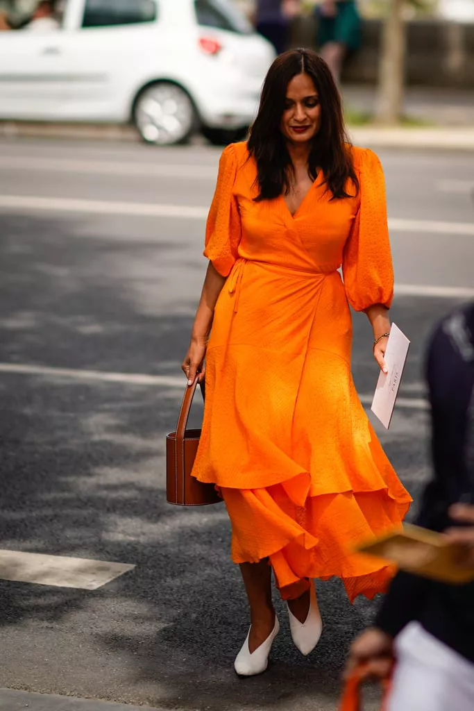 Девушка в ярком оранжевом платье миди, белые туфли и сумка ведро