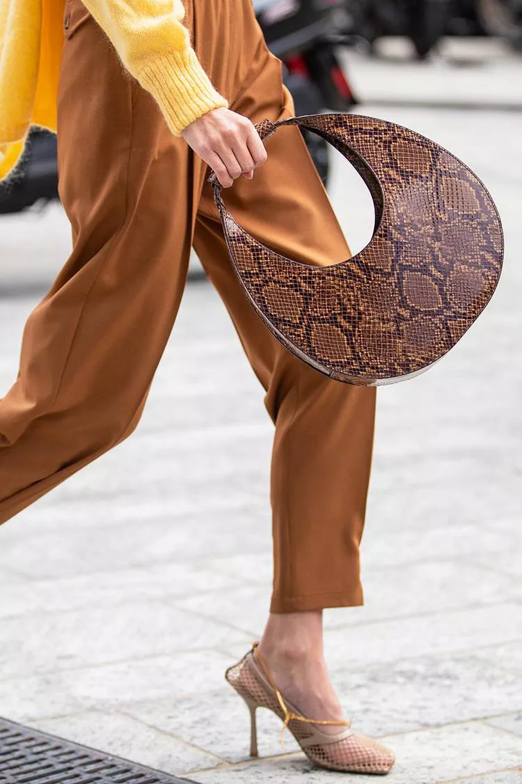Девушка в кориневых брюках, бежевые босоножки и круглая сумка со змеиным принтом