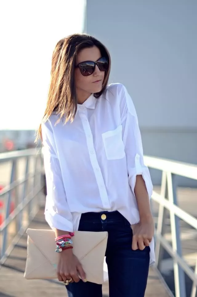 Девушка в синих узких джинсах, белая блузка и бежевый клатч