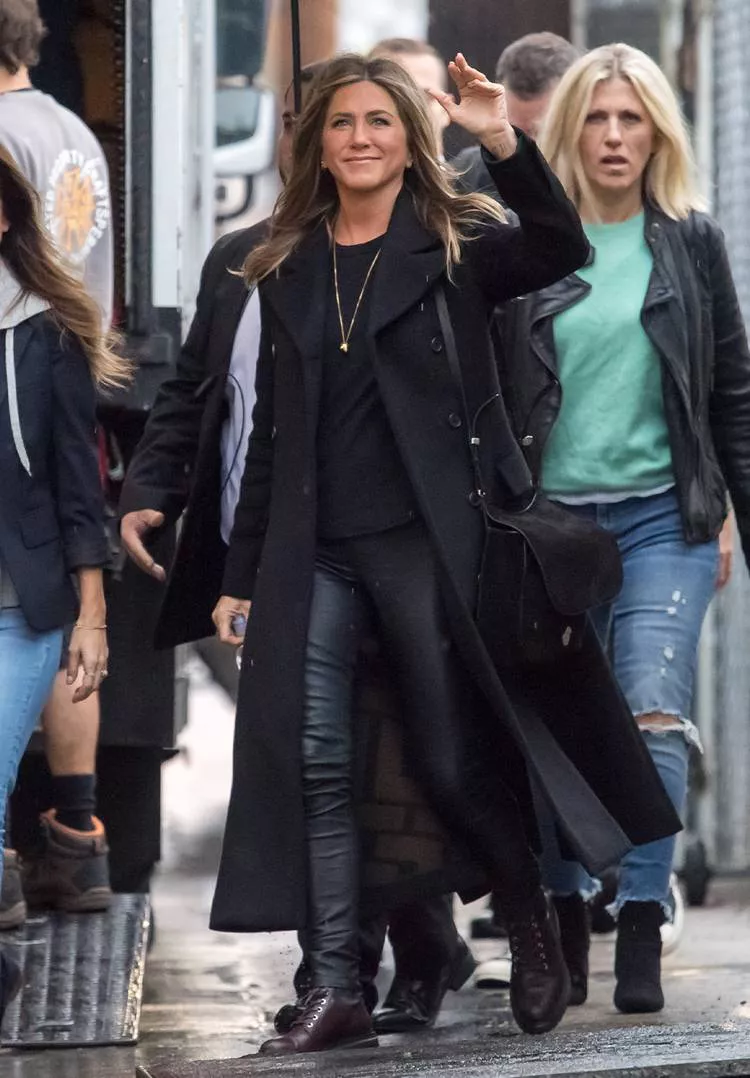 Дженнифер Енистон в черных кожаных лосинах, черное пальто и ботинки на плоской подошве