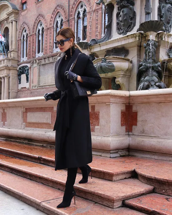Девушка в черном пальто с поясом, сапоги на шпильке и сумочка
